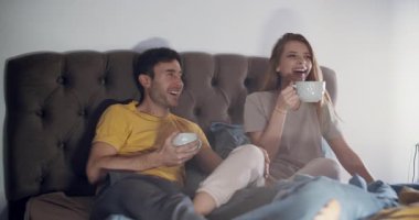 Mutlu bir çift yatakta dinlenir, birlikte eğlenirken atıştırmalıkların ve içkilerin tadını çıkarır.