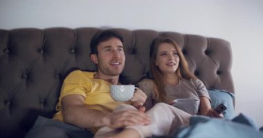 Sıcak bir çift, birlikte film izlerken yatakta dinlenmeyi, kahveyi yudumlamayı ve mutlu bir şekilde gülümsemeyi sever.