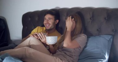 Bir çift, sıcak ve davetkar bir ortamda, kahkahalarımızı ve lezzetli atıştırmalıklarımızı paylaşarak, sıcak bir film gecesinin tadını çıkarıyor.