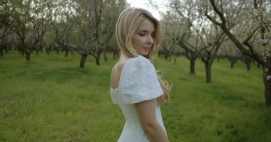 Akan beyaz elbiseli genç bir kadın canlı bir meyve bahçesinde huzur içinde duruyor, doğanın güzelliğini kucaklıyor.