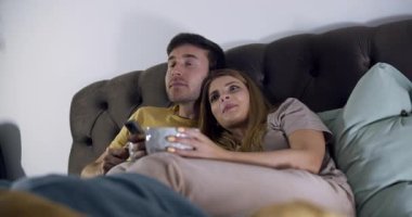 Bir çift kanepelerinde kıvrılıp, atıştırmalıklarını paylaşarak ve sıcak bir atmosfer yaratarak rahat bir film gecesinin tadını çıkarıyor.