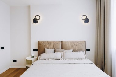 Rahat bir yatak odası, şık bir komodin ve aydınlanma için duvara monte edilmiş iki çekici ışık.