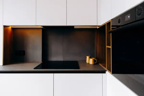 Bu şık mutfak, minimalist elementlerin, karanlık yüzeylerin ve sıcak ışık aksanlarının güzel bir karışımını sergiliyor.