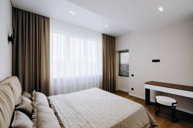 Rahat bir yatak odası, şık bir masa, zarif perdeler ve doğal ışık alan güzel bir pencere.