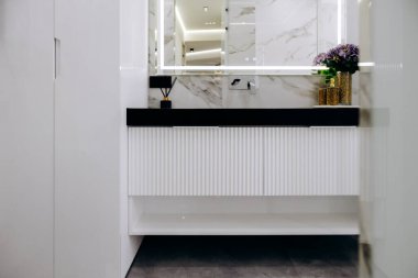 Bu çok güzel tasarlanmış bir banyo şık bir lavabo, zarif bir ayna ve tezgahı süsleyen canlı çiçekler içeriyor.
