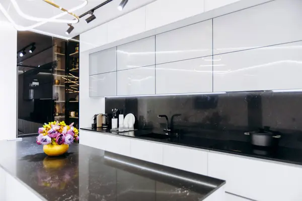 Burası zarif beyaz dolapların olduğu, şık siyah tezgahlarla eşleştirilmiş güzel bir mutfak ve tezgahın üzerine renkli çiçeklerle dolu canlı bir kase, neşe katıyor.