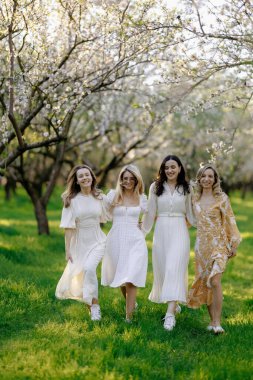 Göz kamaştırıcı beyaz elbiseler giymiş bir grup güzel kadın canlı bir parkta birlikte mutlu bir şekilde yürüyorlar.