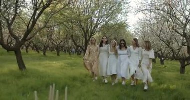 Zarif beyaz elbiseler giyen, güzel meyve bahçesi manzarasının tadını çıkaran neşeli kadınların büyüleyici bir araya gelmesi.