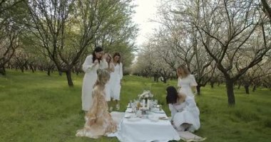 Güzel bir meyve bahçesinin gür güzelliğinin arasında şık bir pikniğe katılan hoş ve neşeli bir arkadaş toplantısı.