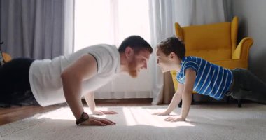 Bir adam ve küçük bir çocuk birlikte şınav çekerek eğlenceli bir antrenmanı paylaşıyorlar. Neşeli etkileşimleri fitness, bağlanma ve sağlıklı bir yaşam tarzını vurguluyor.