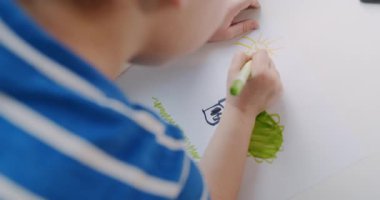 Genç bir çocuk yaratıcılığa dalıyor, kağıt, duvar ve tahtaya kalemler çiziyor, neşeli hayal gücünü ve neşesini sergiliyor.