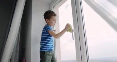 Genç bir çocuk, pencereyi özenle bir bezle temizliyor. Camların gün ışığında ışıldamasını sağlıyor.