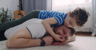 Bir baba ve oğul yerde şefkatli bir anı paylaşıyor, neşe içinde birbirlerine bağlanıyorlar ve birbirlerinin sevgi dolu ilişkilerini ve neşelerini vurguluyorlar