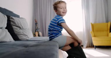 Yürek ısıtan bir video, genç bir çocuğu oturma odasında gösteriyor. Pantolonunu giyer, dost canlısı bir kediyle oynar ve neşeyle zıplar.