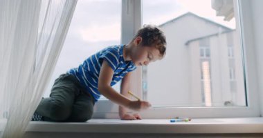 Bir çocuk, yumuşak ışıkla vurgulanan parlak hayal gücünü göstermek için kalem ve kalemlerle pencere pervazında yaratıcı alanında neşe bulur.