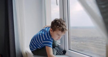 Genç bir çocuk pencere eşiğinde oturuyor, dürbünle dünyayı seyrediyor, manzarayı keşfediyor ve masumiyeti yansıtan bir macera hayali kuruyor.
