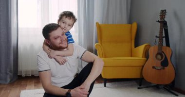 Sıcak bir oturma odasında, neşeli bir çocuk babasının omuzlarına biniyor, bağlarını ve şakacı doğalarını yürekli bir anda sergiliyor