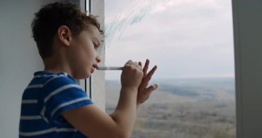 Bu videoda, genç bir çocuk yaratıcı bir şekilde bir kalemle pencereye resim çiziyor, sonra dışarı bakarken dişlerini fırçalıyor, çocukluk masumiyetini gösteriyor.