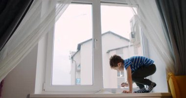 Genç bir çocuk pencere eşiğinde oturmuş, dünyayı seyrediyor. Huzurlu bir atmosferde yaratıcı bir şekilde çizer, temizler ve hayal gücünün parlamasına izin verir.