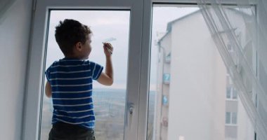 Okyanustan büyülenmiş bir çocuk pencereden dışarı bakıyor. Dalgaları gözlemliyor, pencereyi temizliyor, merakı sorumlulukla harmanlıyor.