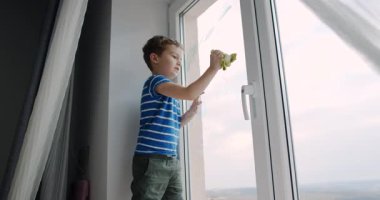 Genç bir çocuk bir bez ve süngerle pencereyi temizliyor, temizlik hevesini sergiliyor. Onun kararlılığı uzaya tazelik getirir.