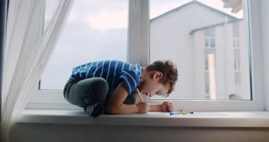 Bu dokunaklı video pencere eşiğinde resim malzemelerine dalmış genç bir çocuğu gösteriyor. Neşeli keşfi güneş ışığıyla artar.