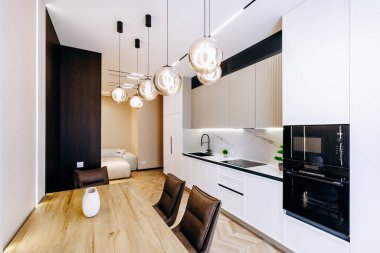 Mutfakta zarif beyaz dolaplar var, dayanıklı ahşap bir masa eşliğinde, sıcak bir atmosfer yaratıyor.