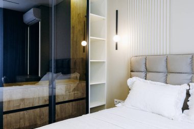 Yatak odasında şık bir aynayla tamamlanmış geniş bir yatak var. Rahatlamak için davetkar bir atmosfer yaratıyor.