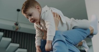 Bir kadın bebek beşiği yapar, sevgi ve şefkat gösterir. Bir adam, bir bebeği omuzlarında taşır ve neşeli bir ebeveyn yakalar. Video aile hayatının neşesini vurguluyor.