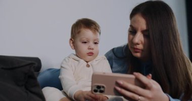 Bu dokunaklı videoda bir anne ve çocuğu rahat bir evde, kanepede kucaklaşıyorlar ve bir tabletin üzerinde kaynaşıyorlar, yanında da neşeli bir kedi var.