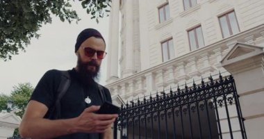 Bu videoda, sakallı bir adam şehir ortamında geziniyor, telefonunu kullanarak teknolojinin ve günlük yaşamın karışımını gösteriyor.