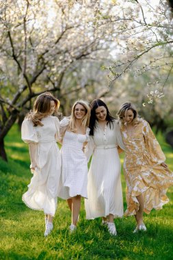 Enfes bir grup kadın, zarif beyaz elbiseler içinde güneşli bir günde zarif bir şekilde güzel bir parkta geziniyorlar.