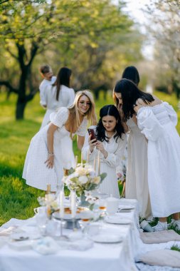 Zarif beyaz elbiseler giymiş fotojenik bir grup kadın güzel dekore edilmiş bir masanın etrafında toplandı.
