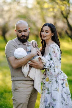Bir erkek ve bir kadın güzel bir bebeği güzel bir parkta nazikçe tutuyorlar, aile olarak birlikte vakit geçiriyorlar.