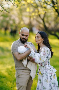 Yeşilliklerle dolu güzel bir parkta, bir erkek ve bir kadın keyifle bebeği bir arada tutarken keyifli bir günün tadını çıkarıyorlar.
