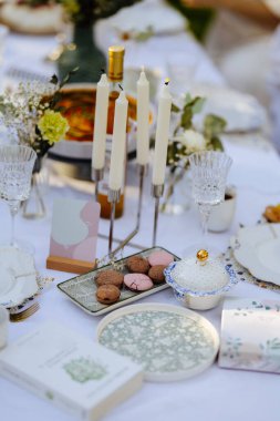 Tabakların, mumların, canlı çiçeklerin ve düşünceli bir şekilde yerleştirilmiş ilginç bir kitabın olduğu güzel bir masa.