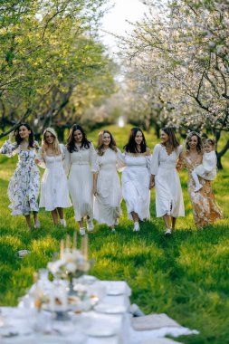 Zarif beyaz elbiseler giymiş neşeli bir grup kadın güzel bir parkta birlikte yürüyorlar, çevrelerindeki güzel manzaranın tadını çıkarıyorlar.