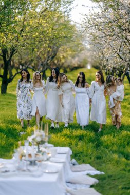 Akan beyaz elbiseler içinde zarif giyinmiş bir kadın topluluğu güzel bir parkta birlikte yürüyor ve manzaranın tadını çıkarıyor.