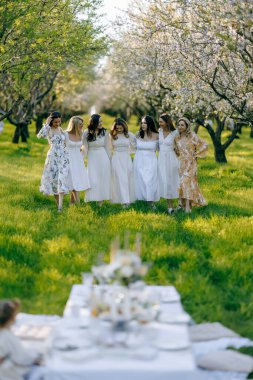 Zarif beyaz elbiseler giymiş hoş bir grup kadın, güzel bir masanın etrafında toplanmış güzel bir tarlada.