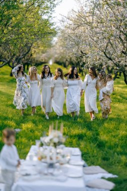 Güzel beyaz elbiseler giymiş bir grup güzel kadın güneşli bir parkta mutlu bir şekilde yürüyorlar.