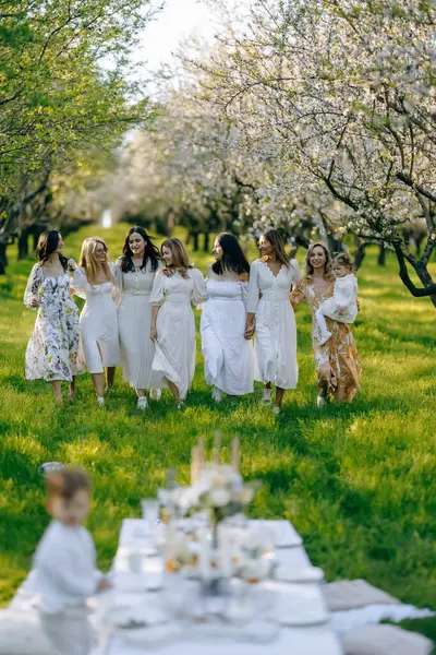 Hoş bir grup kadın zarif bir şekilde parkta yürüyorlar ve zarif beyaz elbiseler giyiyorlar. Bu ortamı güzelleştiriyor.