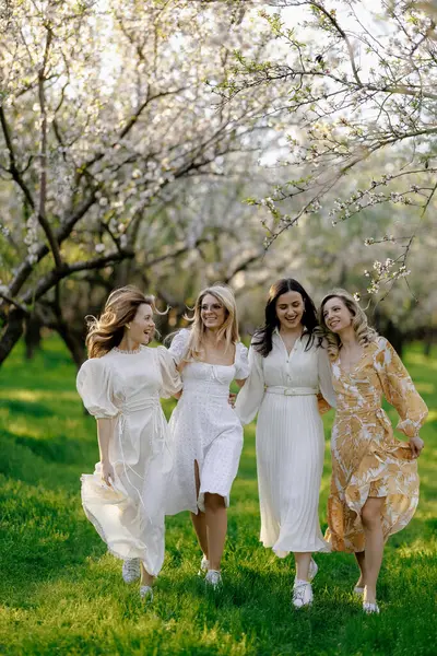 Güzel beyaz elbiseler giymiş bir grup güzel kadın birlikte güzel bir parkta yürüyor ve günün tadını çıkarıyorlar.