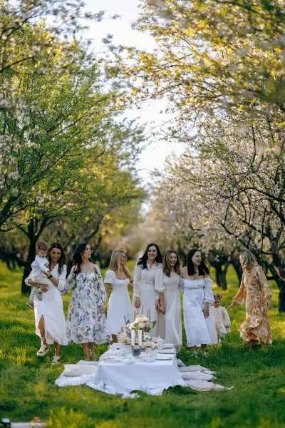 Güzel bir parkta, bir grup kadın vardır, her biri güzel beyaz elbiseler giymiş, zarif bir şekilde hazırlanmış bir masanın etrafında dururlar.