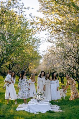 Pahalı bir park ortamında, zarif beyaz elbiseler giyen bir grup kadın birlikte durup dışarıdaki güzel günün tadını çıkarıyorlar.