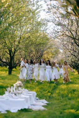 Bahar mevsiminde güzel giyinmiş bir grup kadın neşe içinde el ele tutuşarak bir arada duruyorlar.