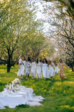 Güzel beyaz elbiseler giymiş güzel bir grup kadın, sıcak bir şekilde el ele tutuşarak resim gibi bir tarlada bir arada duruyorlar.