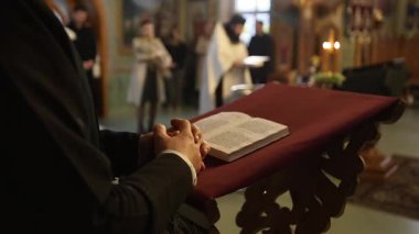 Bir adam, mum ışığı ve saygıdeğer ibadetin atmosferiyle çevrili, dingin bir kilisede, sunakta sessizce İncil okuyor.