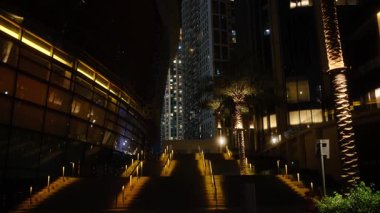 Gece vakti şehir manzarası, şehir yaşamının cazibesini yakalayan canlı bir caddeye dönüşen, yumuşak ışıklı bir binaya giden zarif merdivenleri gösteriyor.