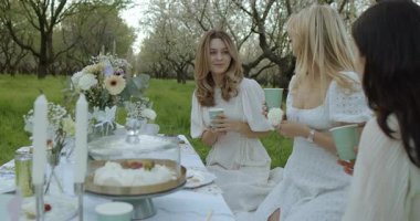 Çiçek açan bir meyve bahçesinde kadınların keyifli bir atmosferde birlikte çay içtikleri hoş bir piknik.