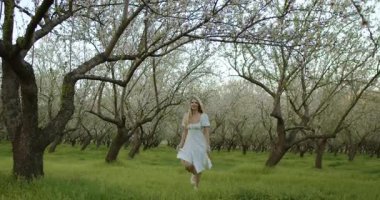 Bir kadın, bahar mevsiminin sakin bir sahnesine dalmış güzel çiçek açan bir meyve bahçesinde zarifçe dolaşır.